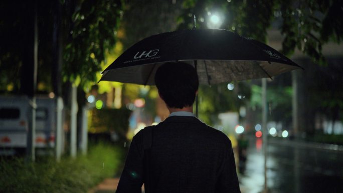 自由职业者在潮湿的天气中带着雨伞在夜晚横穿马路