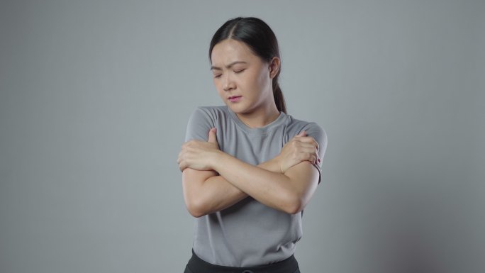 一名亚洲女性因身体疼痛而生病，站在灰色背景下。