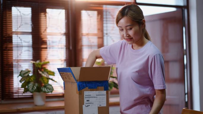 年轻的亚洲女性打开一个订单包，她在网上购买并送货到家