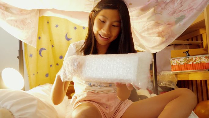 快乐的亚洲女孩在家里用毯子制作的露营帐篷下，从网上购物中购买的开箱商品，生活方式理念。