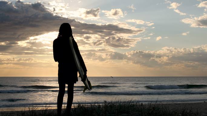 视频肖像非洲澳大利亚女冲浪者在日出时望着冲浪