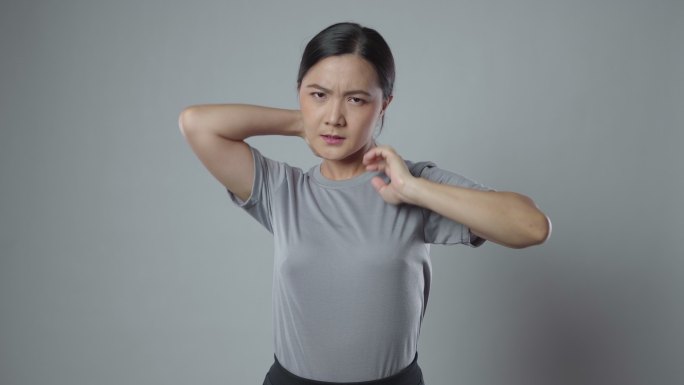 一名亚洲女性因身体疼痛而生病，站在灰色背景下。
