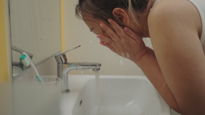 亚洲女人在浴室里把水泼在脸上醒来的侧视图，慢镜头