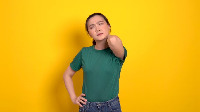 一名亚洲女性因身体疼痛而生病，站在黄色背景上。
