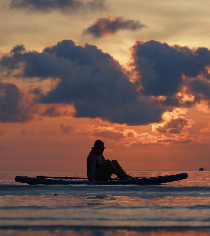 日落时分坐在海上冲浪板上的女人