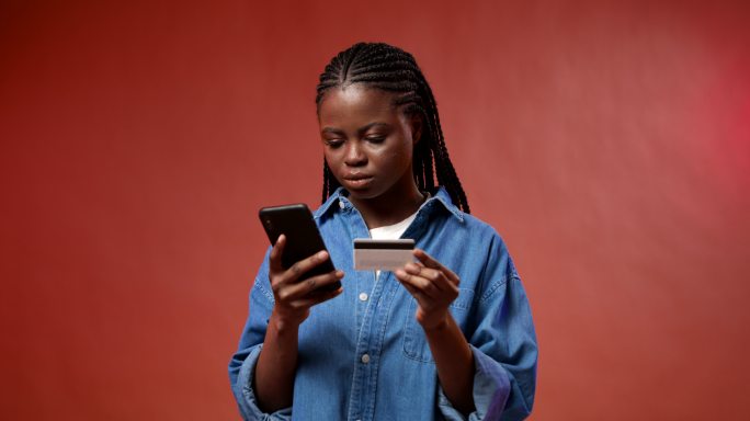 一个皮肤黝黑的年轻学生在智能手机中输入卡号，购买她非常想要的东西