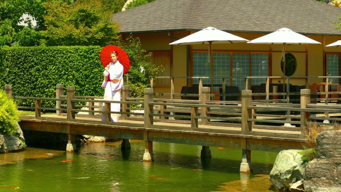 在茶馆附近花园里的桥上，一个穿着和服、打着伞的女人