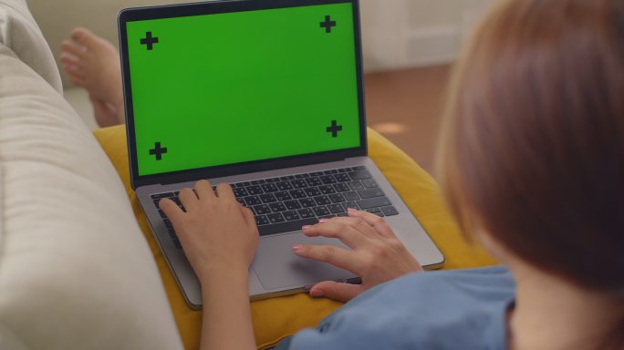 亚洲孕妇在家工作时使用绿色屏幕上的笔记本电脑