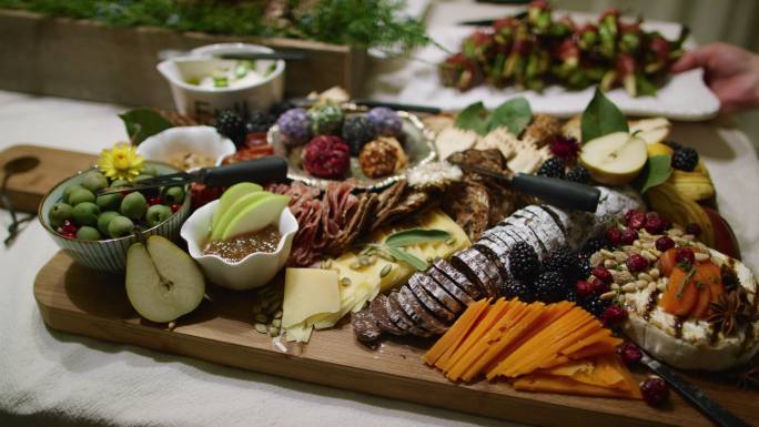 在室内庆典/派对上，一个人将开胃菜放在背景中，而摄像机将开胃菜与各种水果、酱汁和装饰一起放入桌子上的