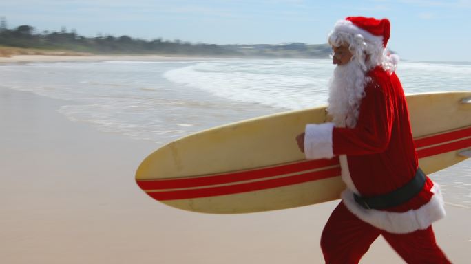 澳大利亚圣诞冲浪圣诞老人带着冲浪板在海滩上跑步