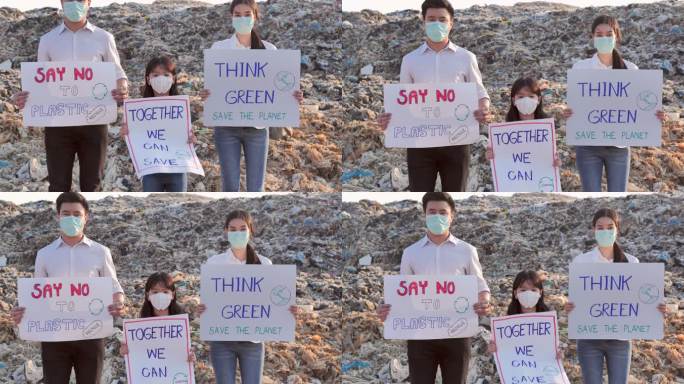 一家三口不同年龄的志愿者站在亚洲垃圾填埋场的巨大垃圾场上，举着为保护自然而战的环保运动积极分子的海报