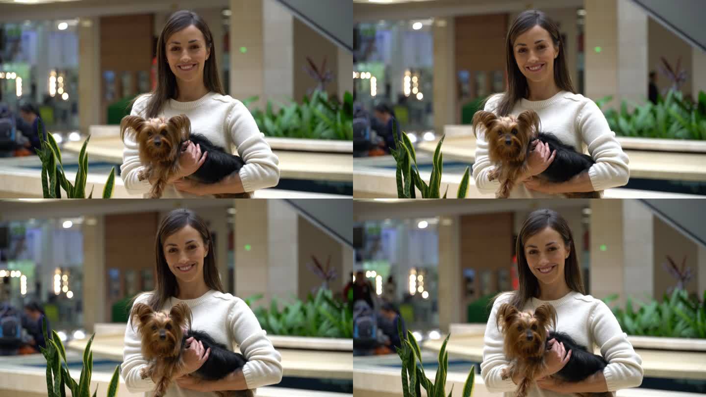商场里的一位拉丁美洲美女抱着她的宠物，面对镜头微笑