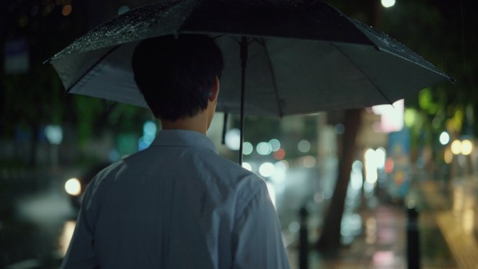 自由职业者在潮湿的天气中带着雨伞在夜晚横穿马路