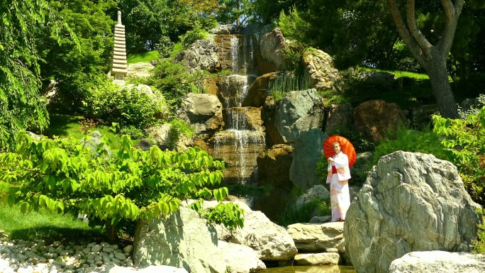 美丽的风景-一个穿着和服的年轻女子在公园里有瀑布的岩石附近