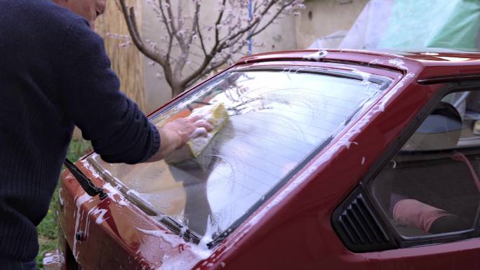 特写一名男子在后院拿着海绵洗车的双手。