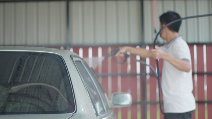 一名亚洲男子在家里用泵上的压力喷雾器洗车