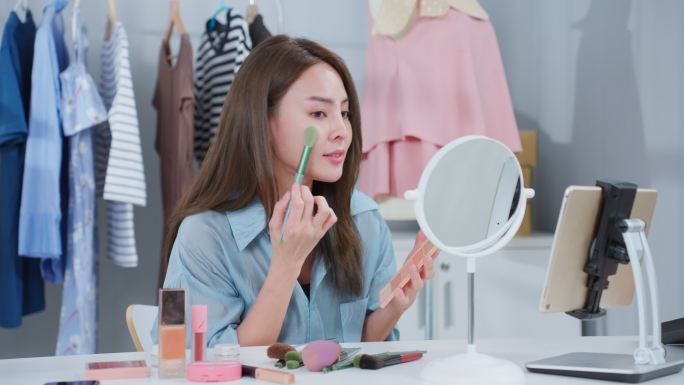 亚洲美女视频记录者在家里对着镜头回顾化妆品。美丽的美妆博主影响力女性直播，并在写字楼商店的平板电脑上