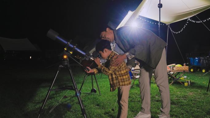 傍晚爸爸和儿子在露营地用望远镜看星空