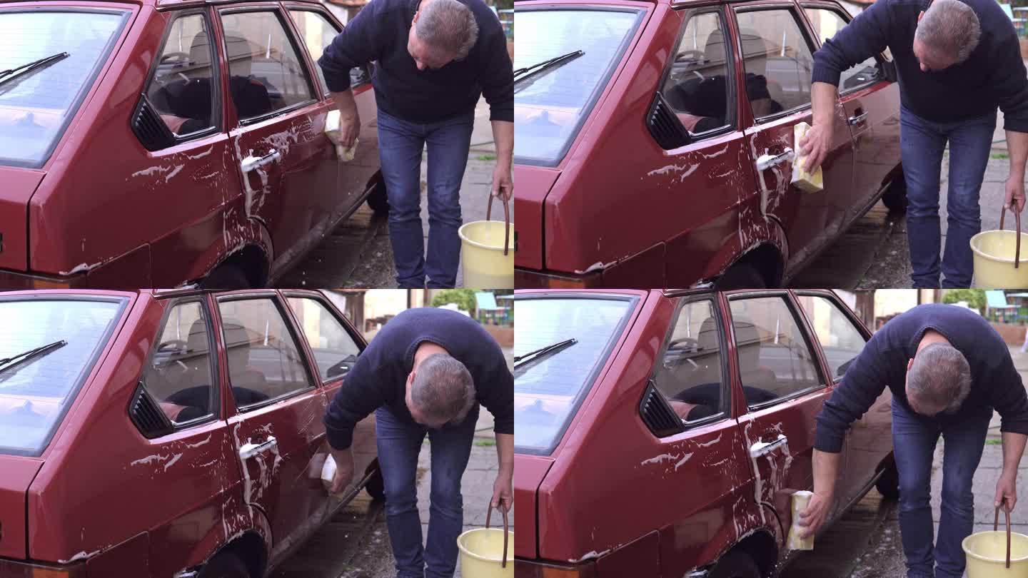 一位老年人在后院拿着海绵洗车。