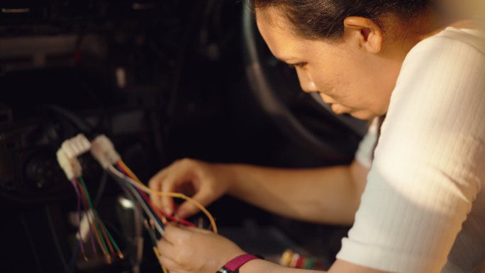 头部镜头：亚洲中年女性搭配汽车电缆，将显示器与汽车内部的数码摄像机连接起来，自己动手