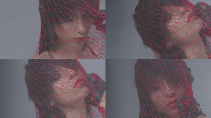 性感的黑发时尚模特被困在红色网中，露出面部表情。时尚视频。