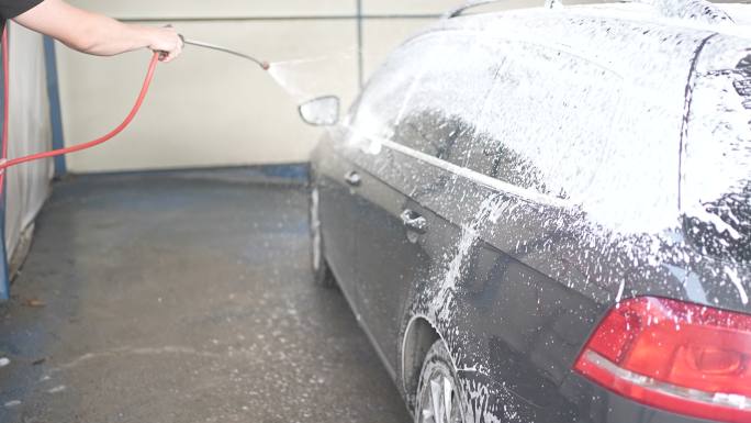男性在洗车前用喷枪在车上喷洒雪沫