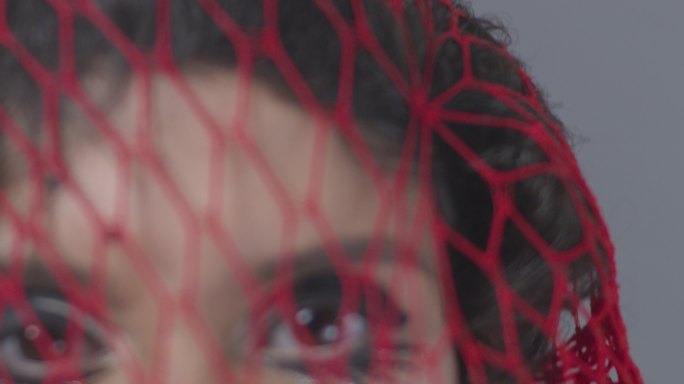 可爱的黑发时尚模特被困在红色网中，露出面部表情。时尚视频。