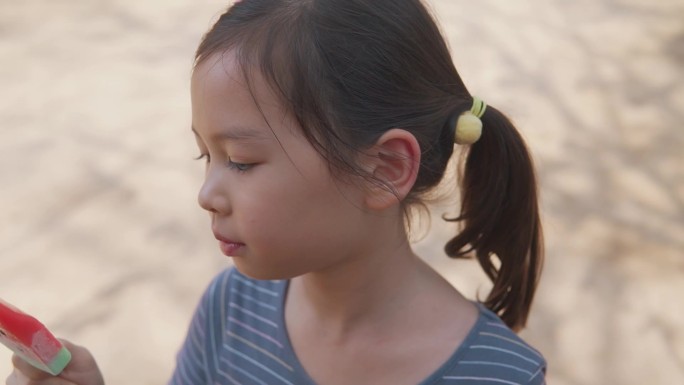 手持慢动作的年轻混血亚洲女孩在炎热的夏季吃西瓜冰棍