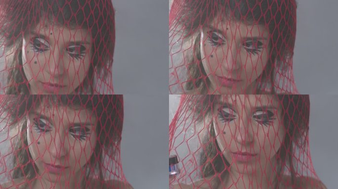 布鲁内特（Brunette）性感时尚模特被困在红色的网里，手里拿着一个蓝色的眼影罐。时尚视频。