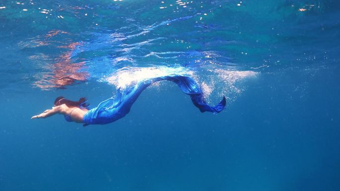 身穿美人鱼裙的亚洲女性在清澈的海水中潜水
