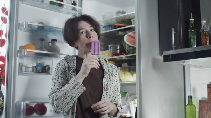 成熟的女人在冰箱旁边吃冰淇淋