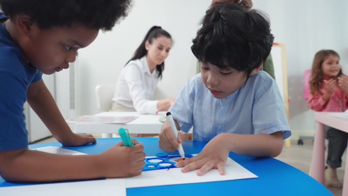 在美术课上，两个亚洲的小学男孩一起用圆尺在白纸上画圆。5-7岁的亚洲男孩正在画画，背景是教室里有很多
