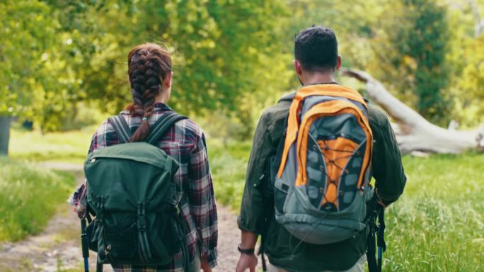 徒步旅行的夫妇在森林小径上散步和交谈。两个合适的背包客探索自然和美丽的风景，在大自然中充满活力的绿草