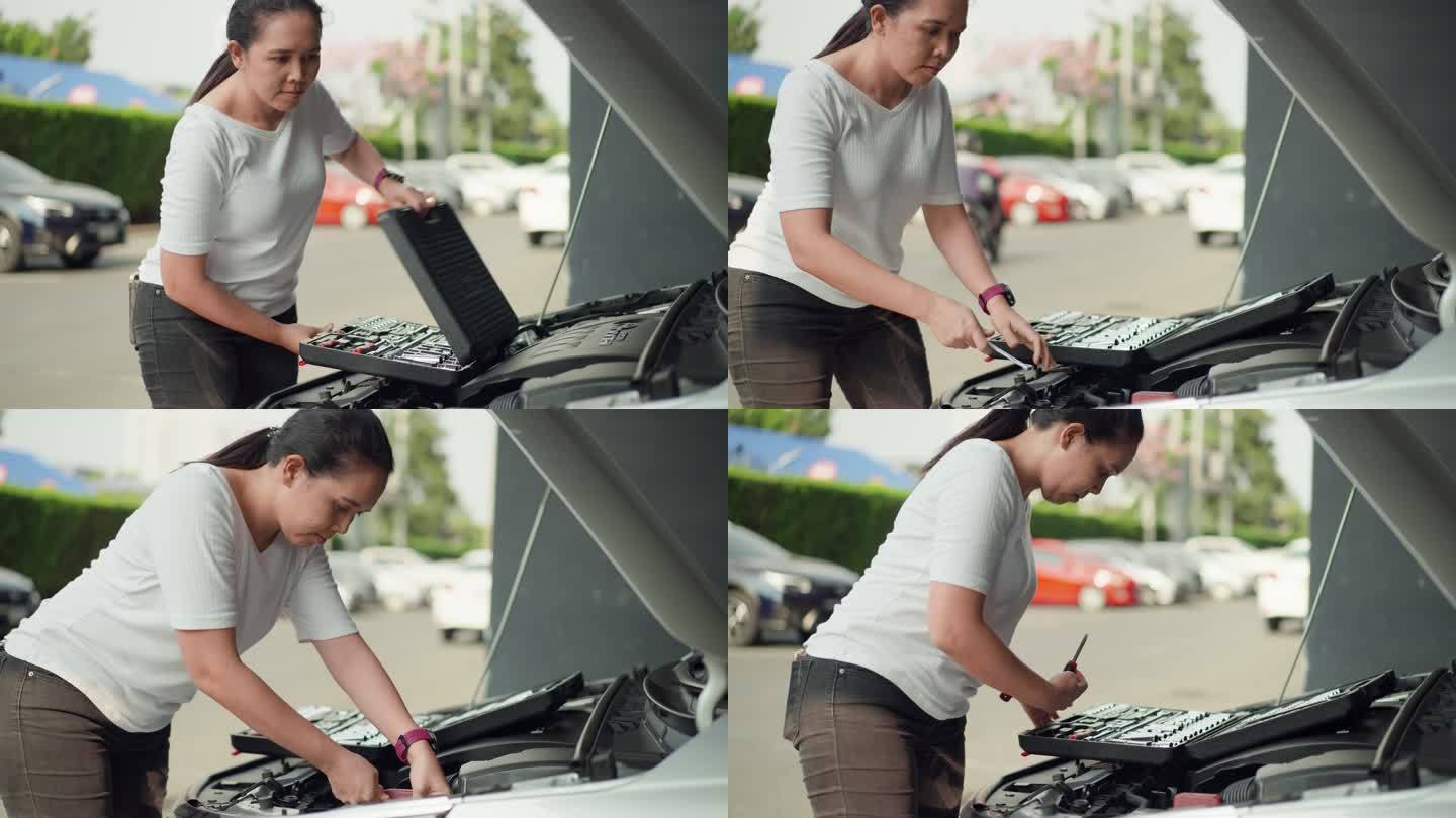 在公寓停车场，一位亚洲中年妇女拿着一个大工具箱，打开、选择并用扳手自己检查汽车电池