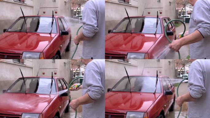 一位老人手里拿着一根软管，在自家后院洗车。