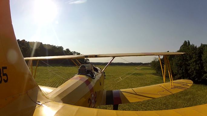 黄色双翼飞机在农田和房屋上空低空飞行