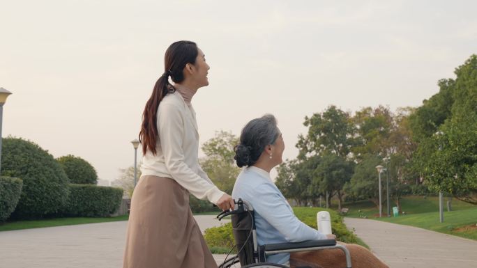 年轻女性推着坐轮椅的母亲公园散步