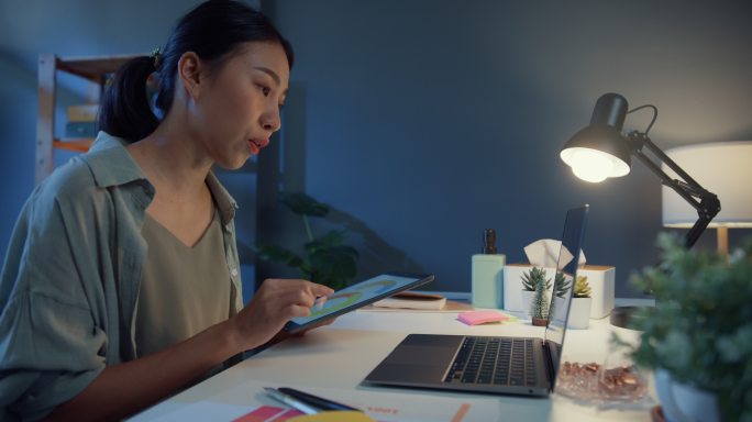 年轻的亚洲自由职业女性晚上在家里的客厅里使用笔记本电脑视频电话会议。