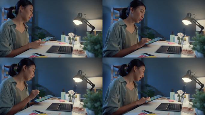 年轻的亚洲自由职业女性晚上在家里的客厅里使用笔记本电脑视频电话会议。