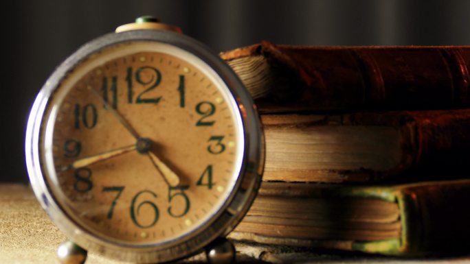 木制桌子上有旧皮革封面书的复古闹钟