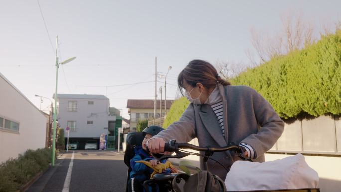 母亲走在街上，推着自行车，儿子坐在自行车后座上