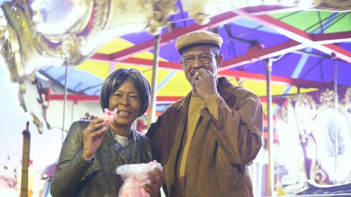 狂欢节上顽皮的老年黑人夫妇吃棉花糖