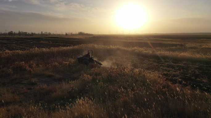 夕阳下农民驾驶拖拉机进行荒地开垦