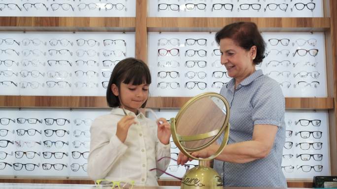 微笑的女孩顾客在眼镜店挑选眼镜