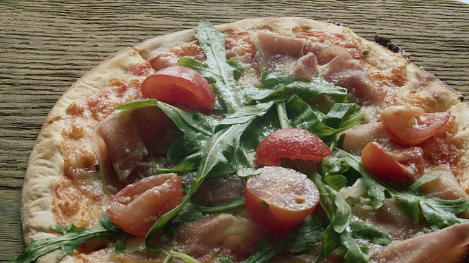 火腿披萨配斯特拉查特拉奶酪、西红柿和芝麻叶。在木桌上旋转