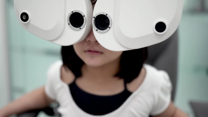 亚洲中国女孩坐在椅子上，在眼科诊所用数码验光仪进行视力测试