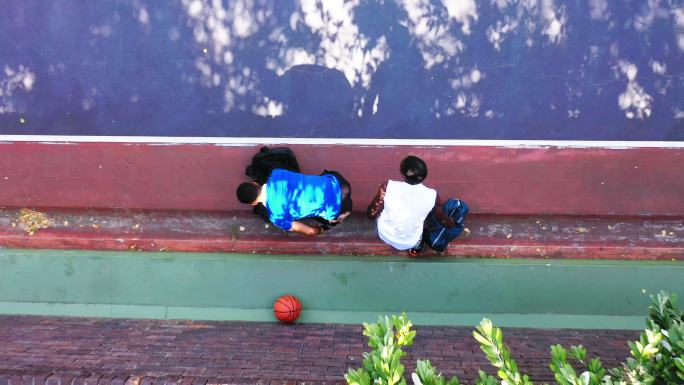两个面目全非的男子在打篮球前坐在板凳上。年轻人从上面玩体育