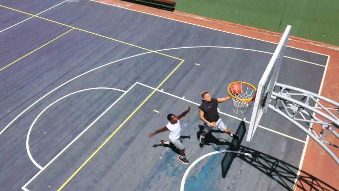 两名男子在打篮球时将球射入篮筐的头顶。年轻人从上面玩体育
