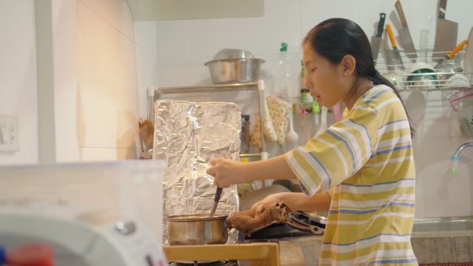 亚洲女孩在家里的厨房里用炉灶做饭，周末生活方式理念。