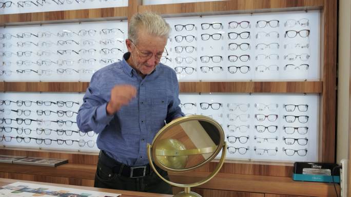 在眼镜店，一位老年男子在镜子前试眼镜